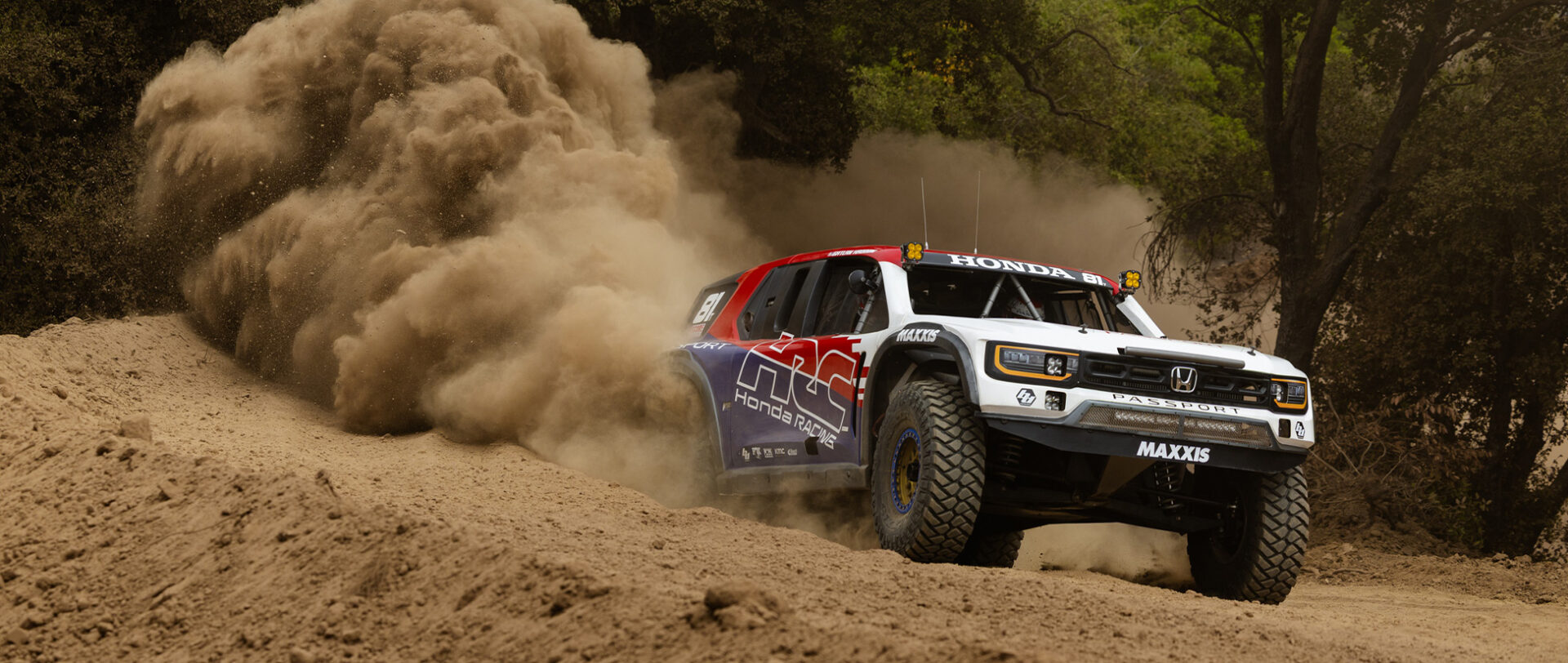 Red white and blue Desert race truck at full speed in the desert with a huge billowing plume of dust from the back wheels.