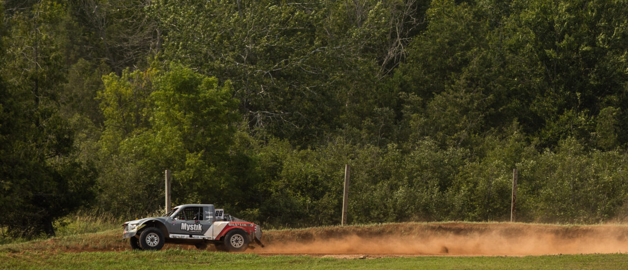 Wide shot of grey and red Pro4 race truck under full acceleration.