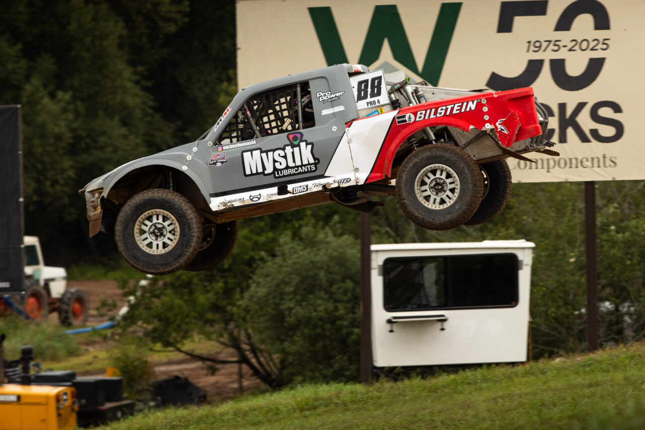 Mickey Thomas in his grey and red Pro4 truck flying through the air over a big jump at Bark River Race course.