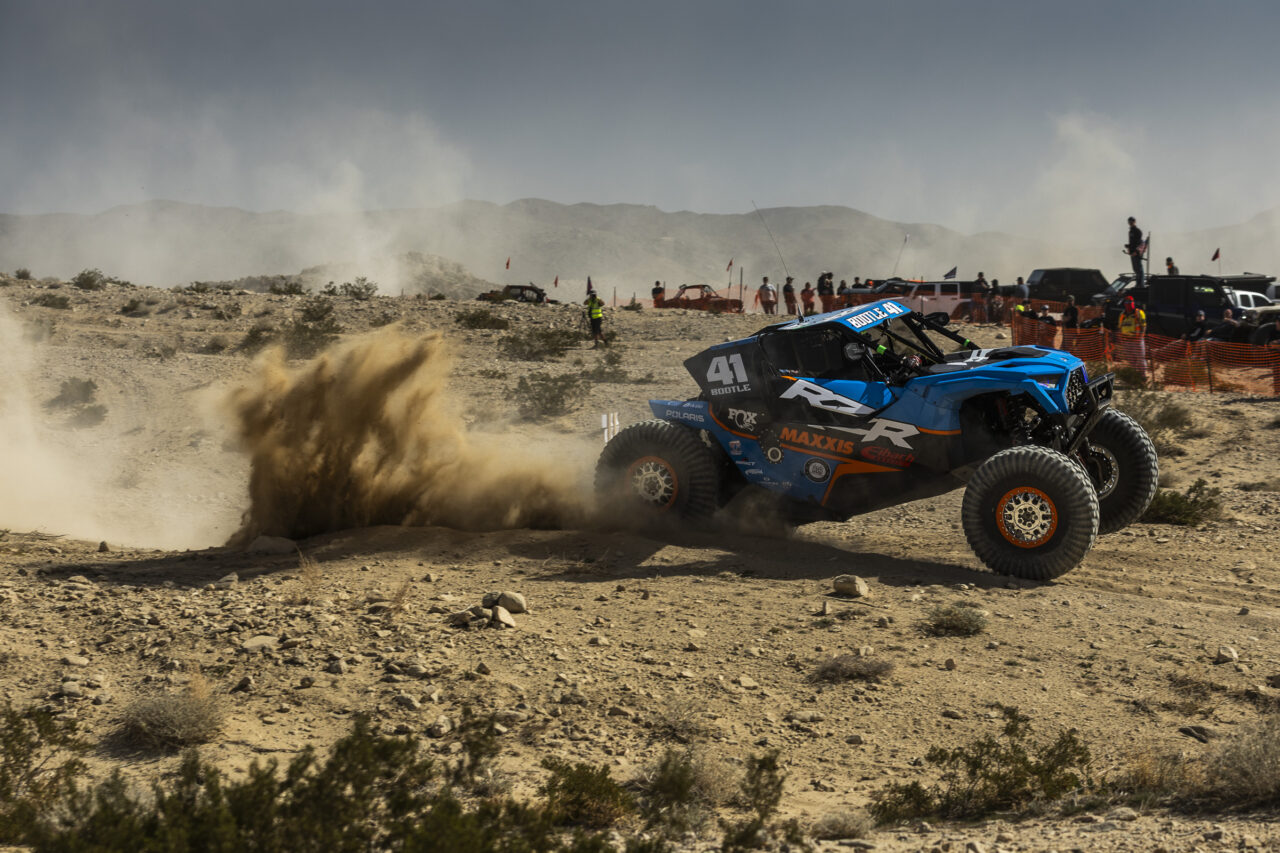 a blue and orange Polaris RZR SxS toting it's front wheels as it sprays sand and silt everywhere while under heavy acceleration.