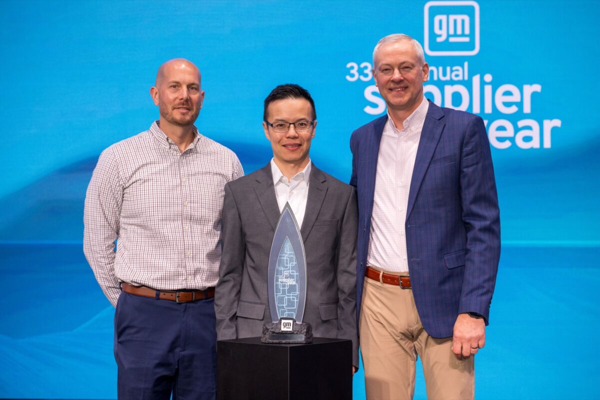 Three men standing behind a GM supplier of the year trophy.
