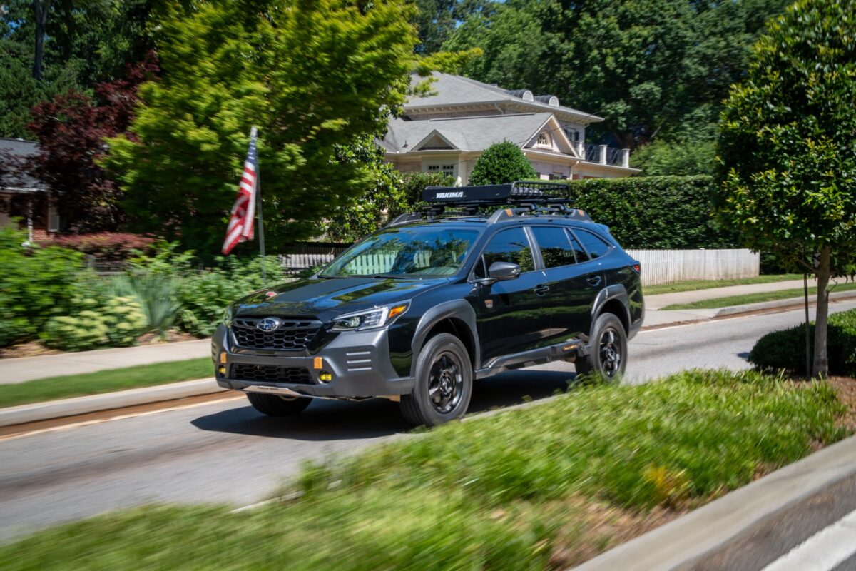 Black Subaru Outback driving down an urban street.