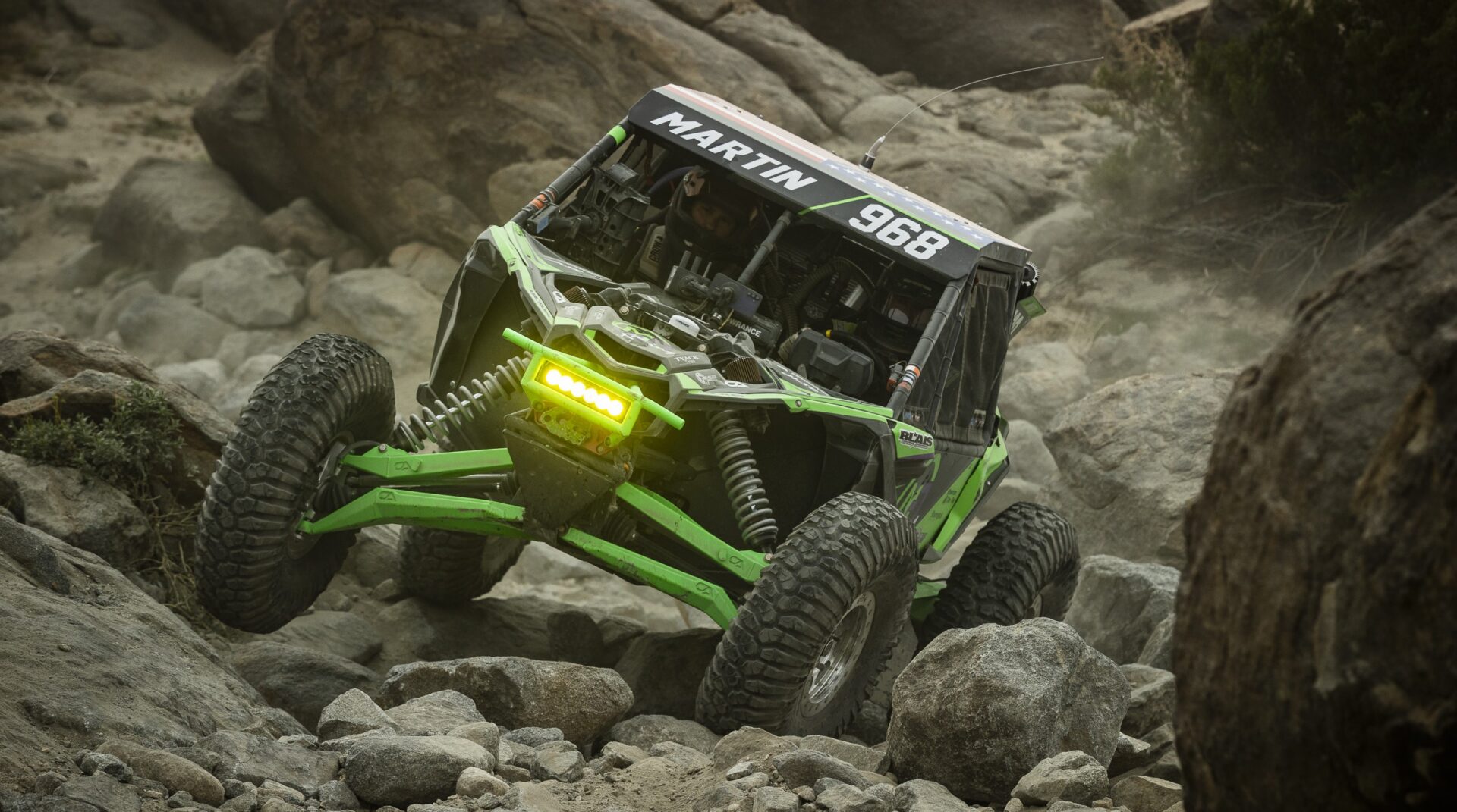 A green and black SxS navigating larger boulders on Maxxis' Super Knobby Roxxzillas.