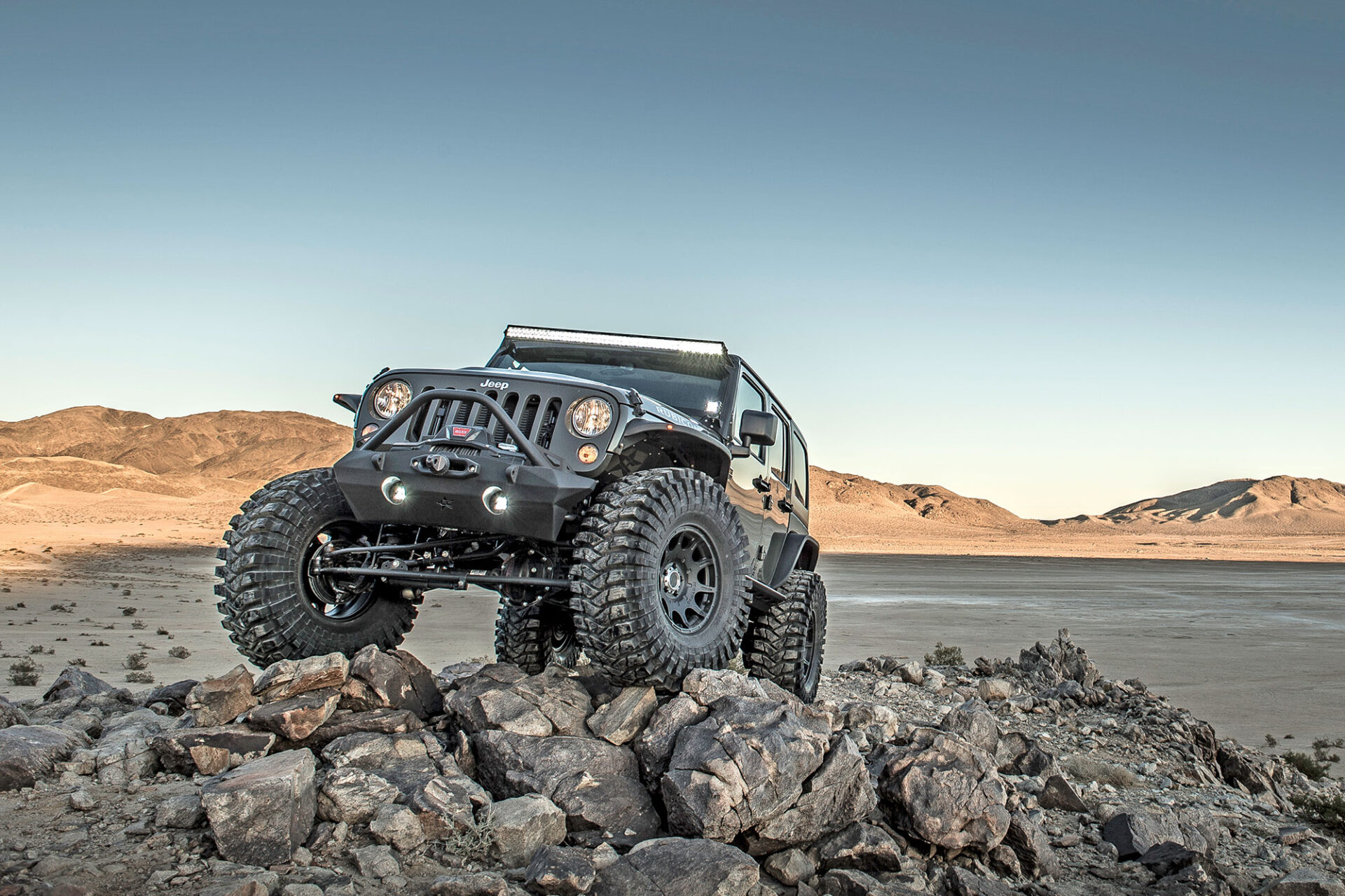 Vehicle outfitted with extreme-off-road Maxxis tires crossing desert rocks.