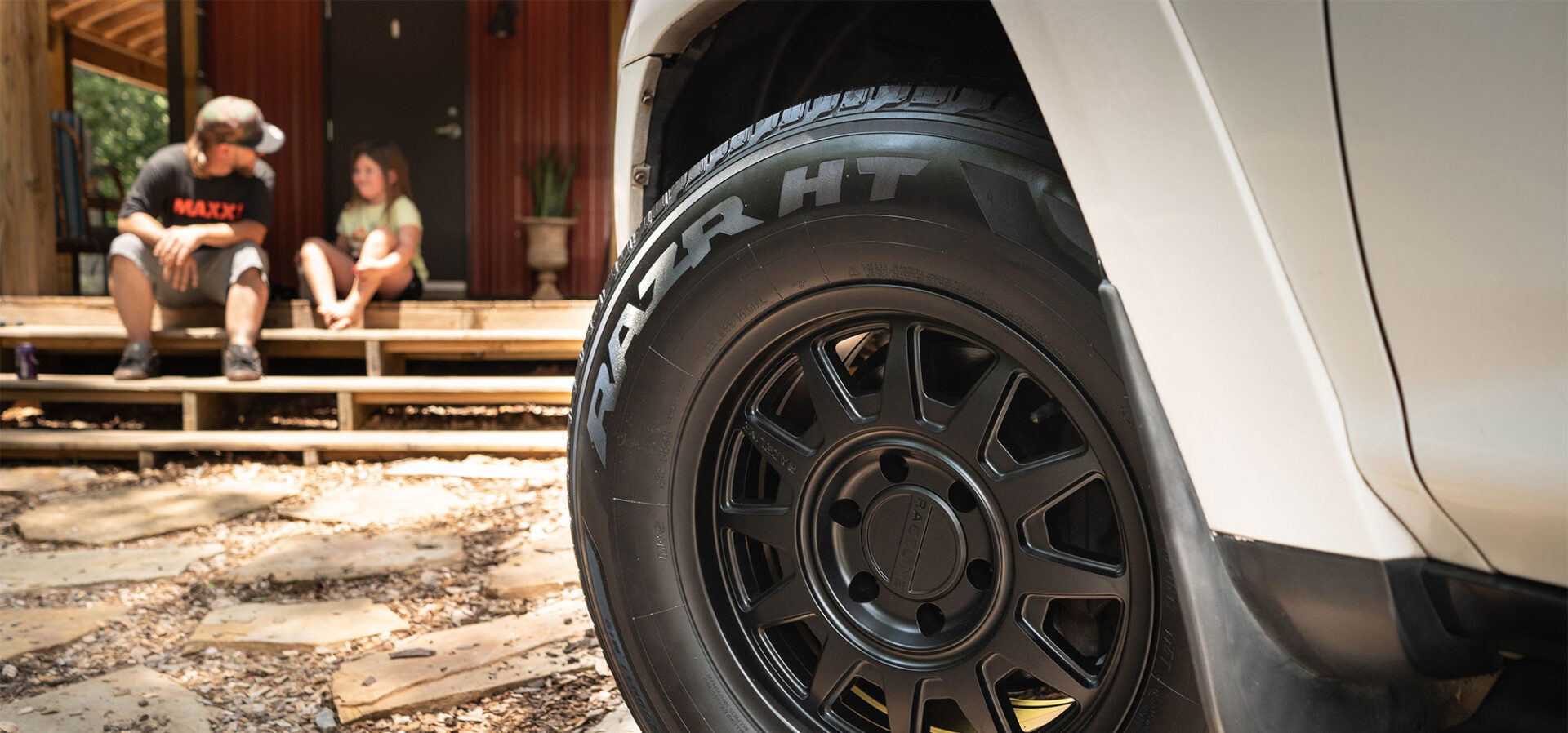 Tight shot of a tire with man and girl sitting on stairs.