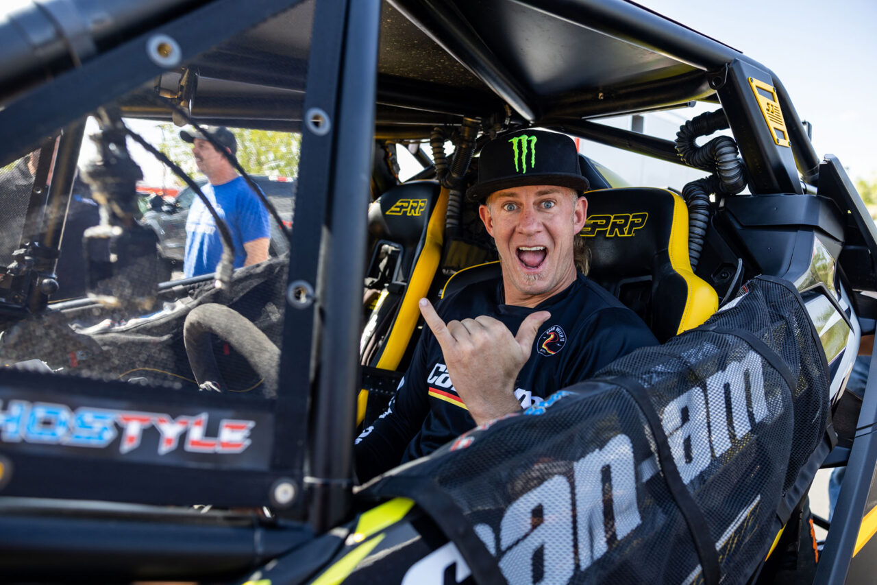 A jubilant Dustin “Battle Axe” Jones in his Can-Am UTV waving a shaka hand gesture to the photographer.