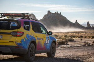 Team #211 Honda Pilot Trail Sport vehicle outfitted with Maxxis all-terrain RAZR AT tires facing off-road terrain with mountains in the background.