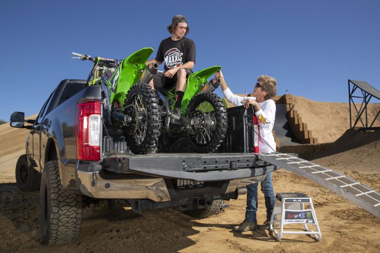 Axell sitting in the back of a truck with his motocross bikes talking to another man