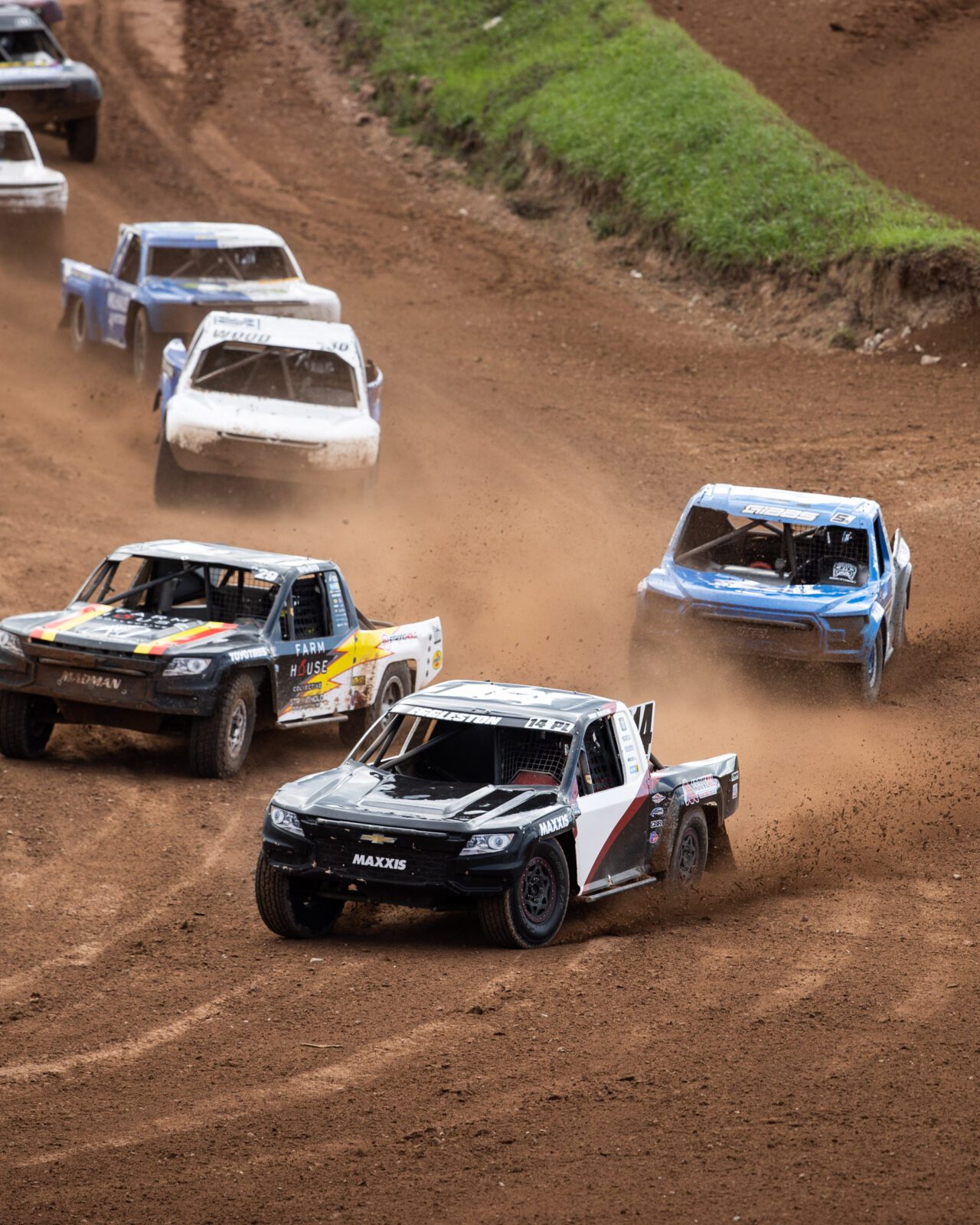White and Black Maxxis race truck leading a pack of pro lite trucks into turn one at Crandon international speedway.