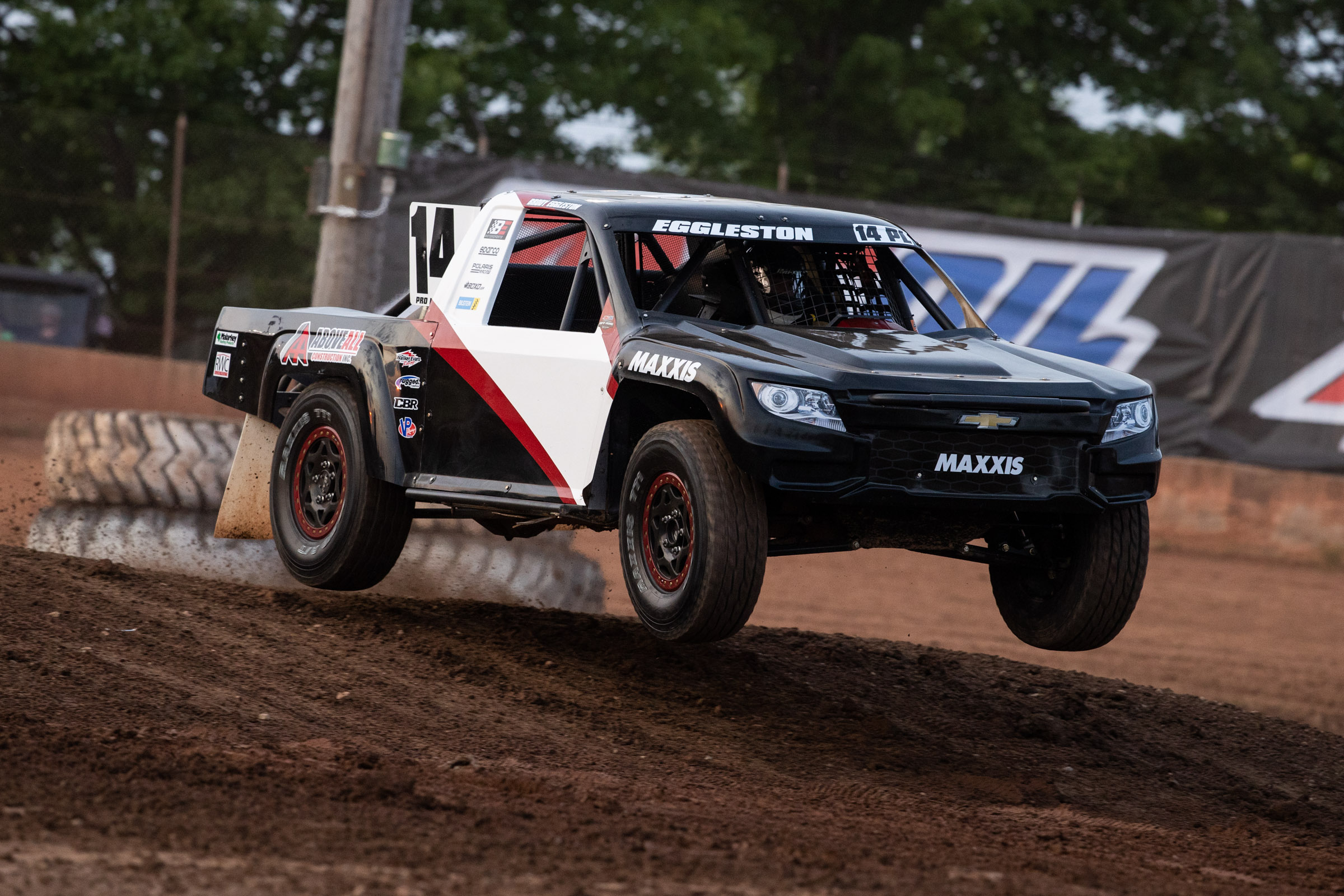 black white and red race truck jumping down a dirt hill