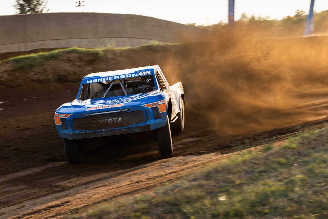 white and blue truck accelerating hard on the dirt racetrack.