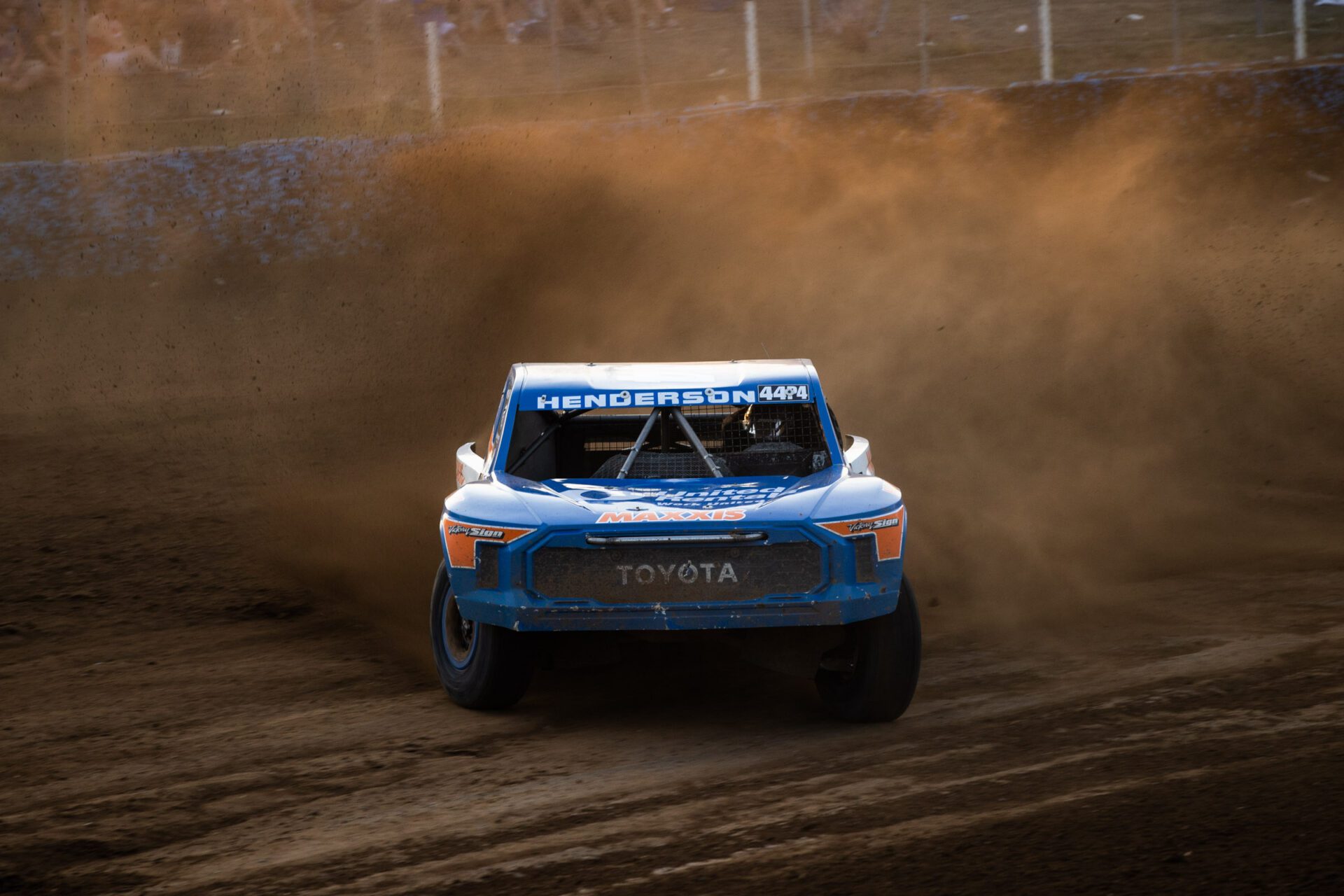 Blue and orange truck blasting around a dirt berm at Crandon Raceway.