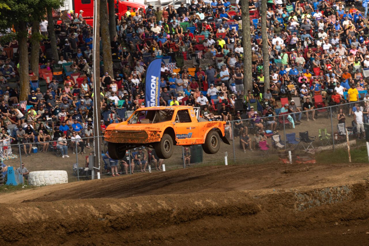 Adrian Cenni Jumping his orange truck through the air in front of a crowd of fans.