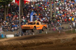 Adrian Cenni Jumping his orange truck through the air in front of a crowd of fans.