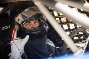 Driver strapped into his race truck, helmet on, making a ready to rock fist while looking at the camera.
