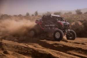 Pink and black SxS at full speed in the desert with large plume of dust trailing behind it.