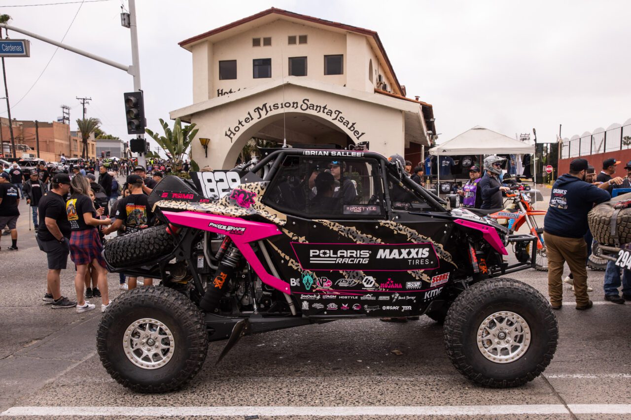 A black and pink SxS sitting in front of a tan building.