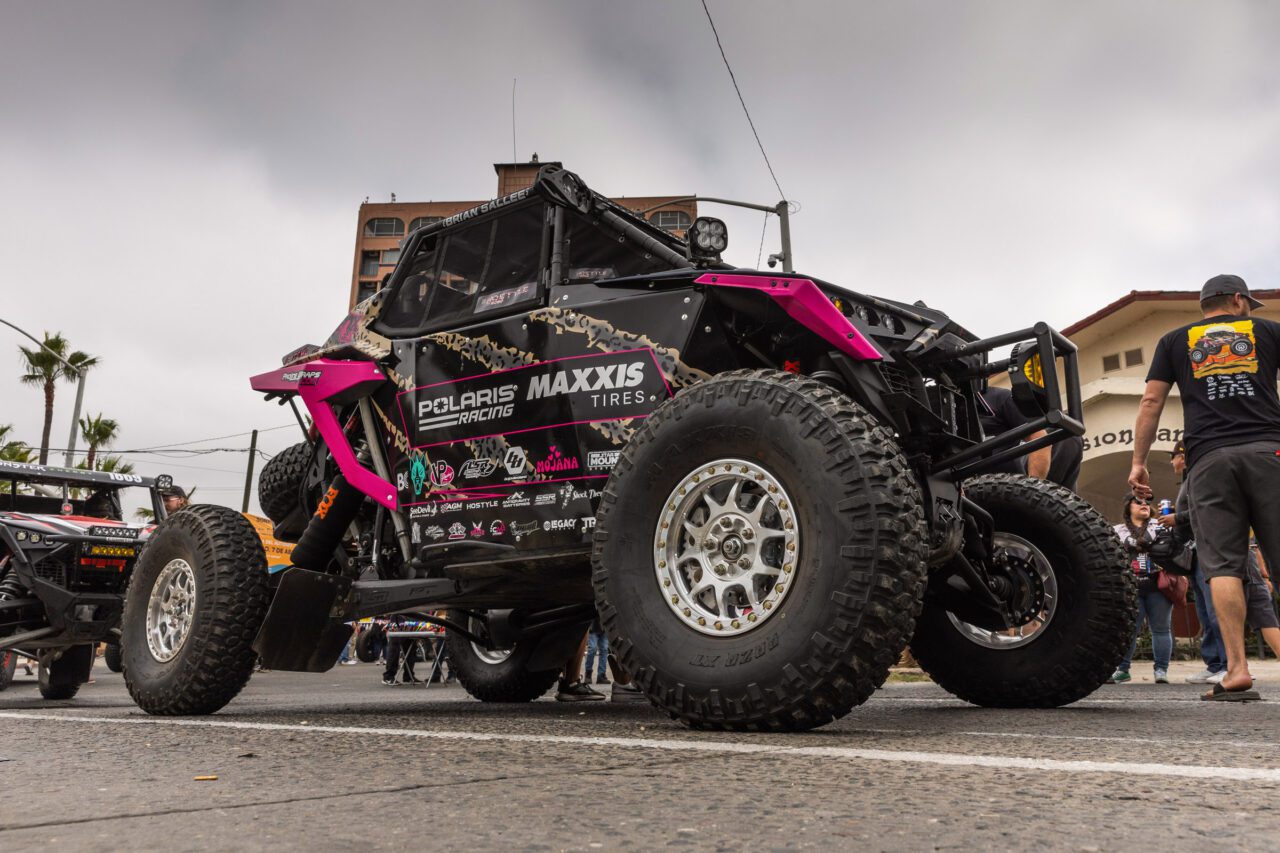 A pink and black SxS staged in an asphalt parking lot with grey skys as a back drop.