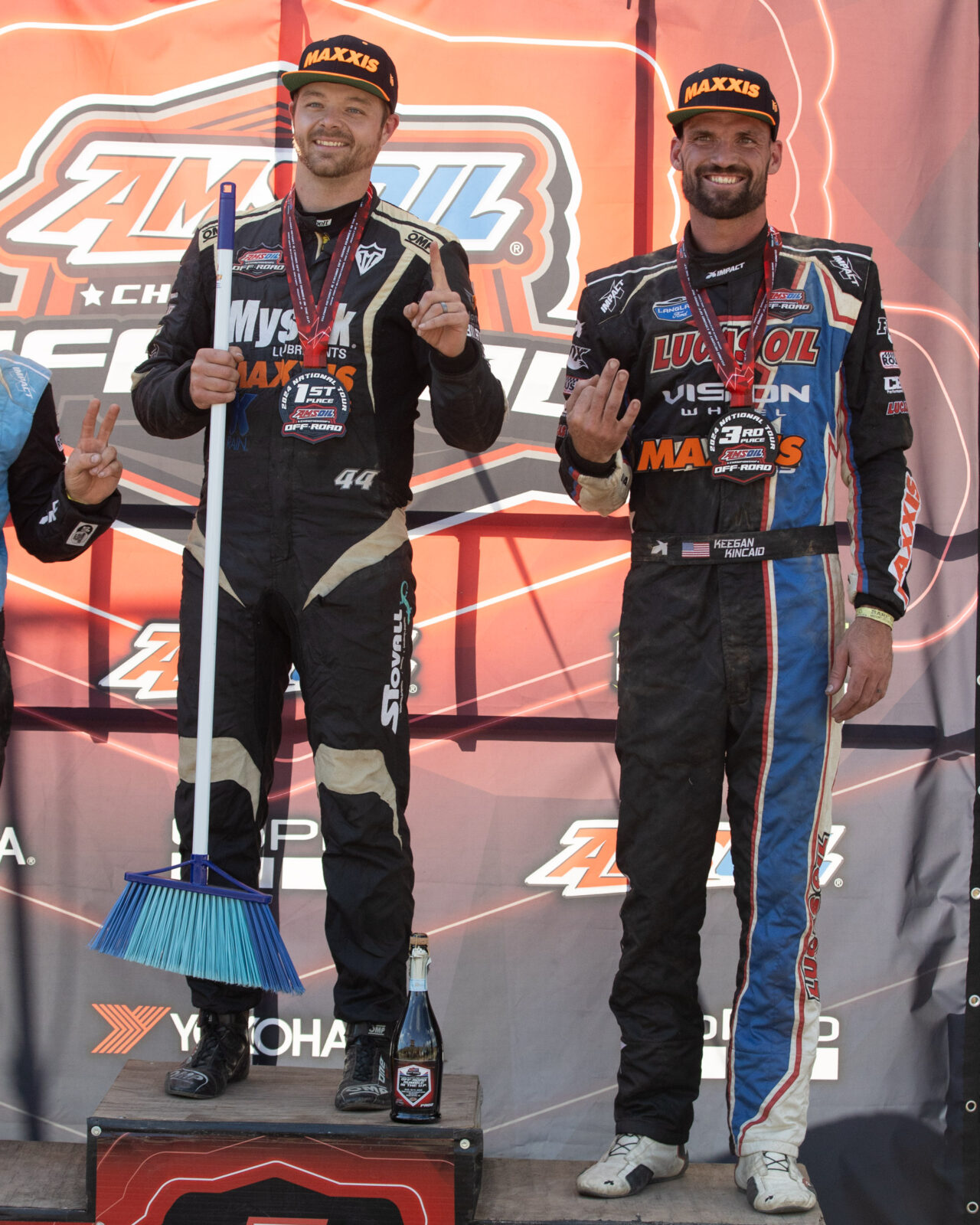 Maxxis athletes on the podium, one holding a broom.