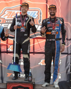 Maxxis athletes on the podium, one holding a broom.