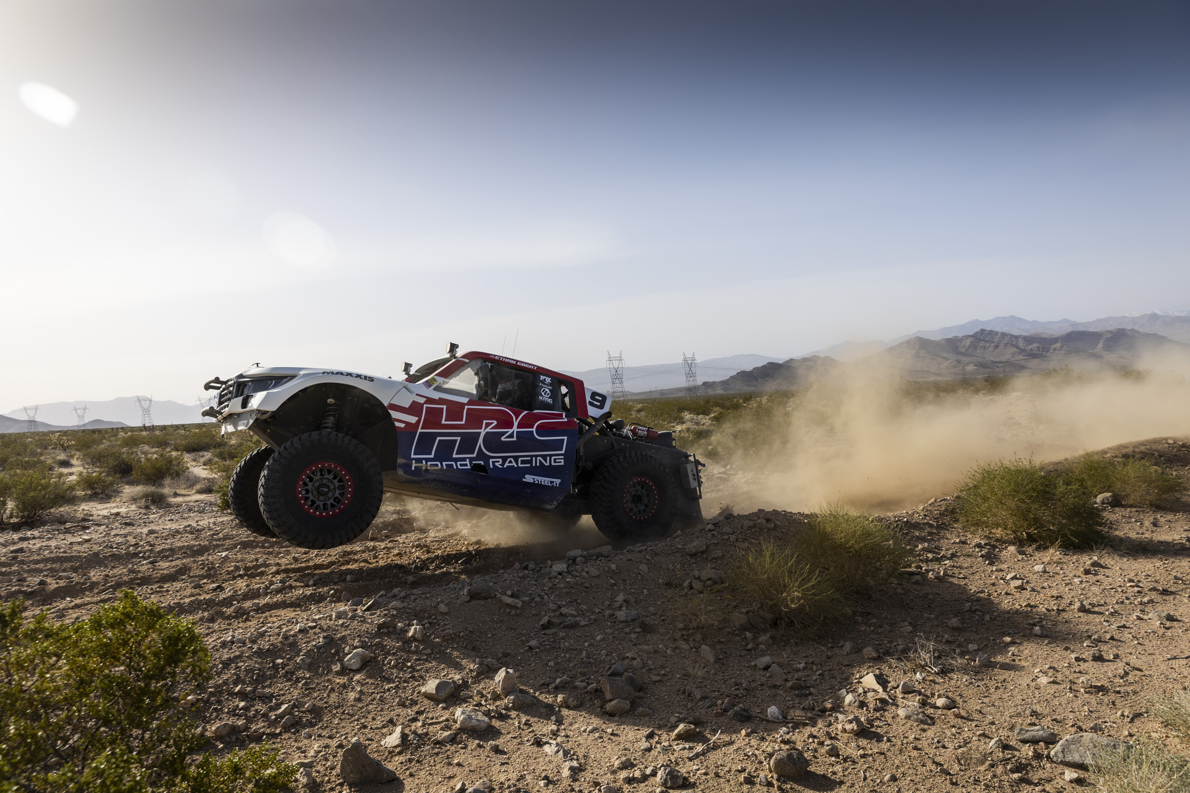 The Factory Off-Road Honda Rigline mid launch off of a hard pack dirt ramp in the desert.