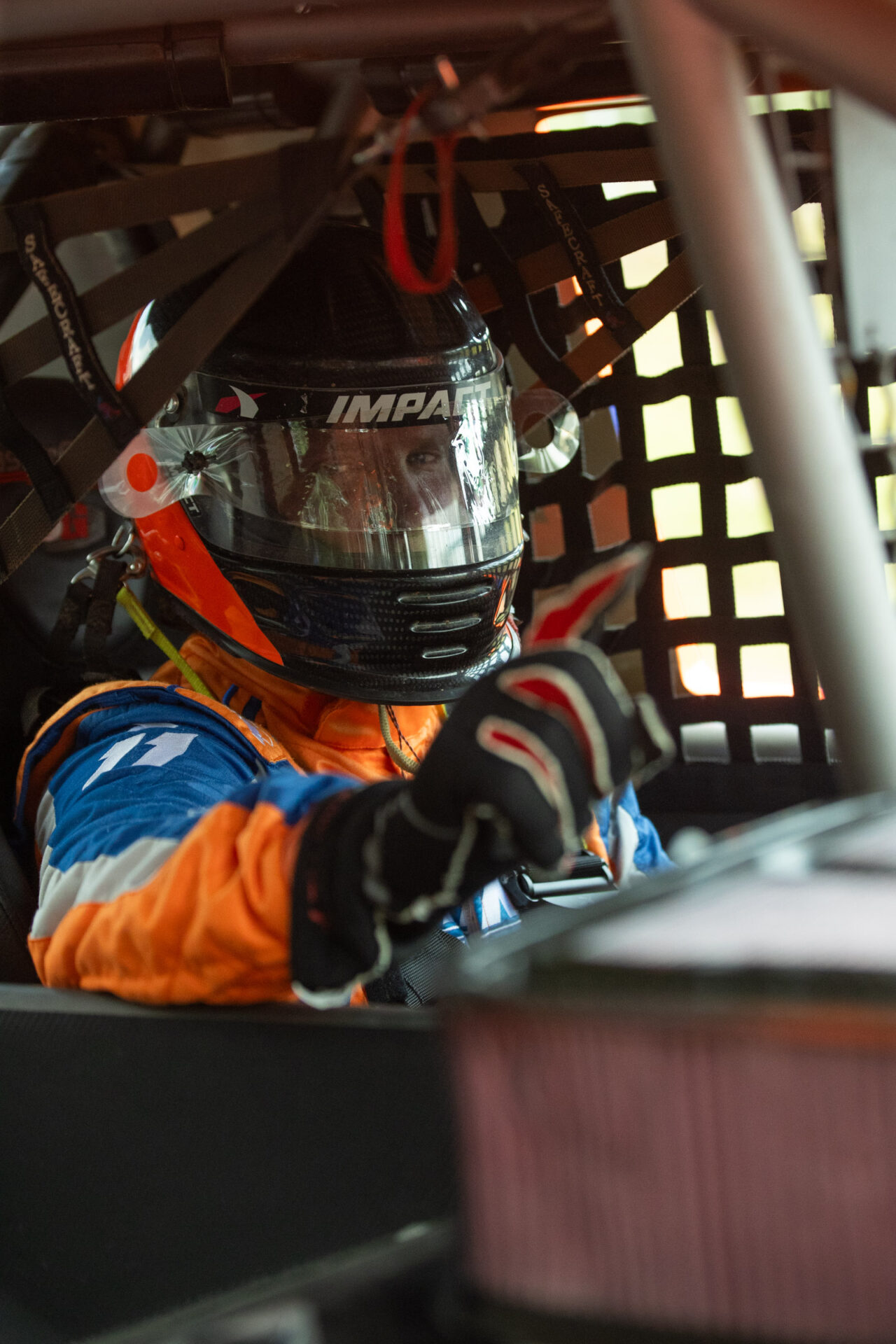 Adrian Cenni strapped in to his race truck looking at the camera and holding up a 