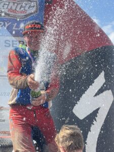 Hunter Hart spraying a bottle of Champ at the Camera on the podium of a gncc race.