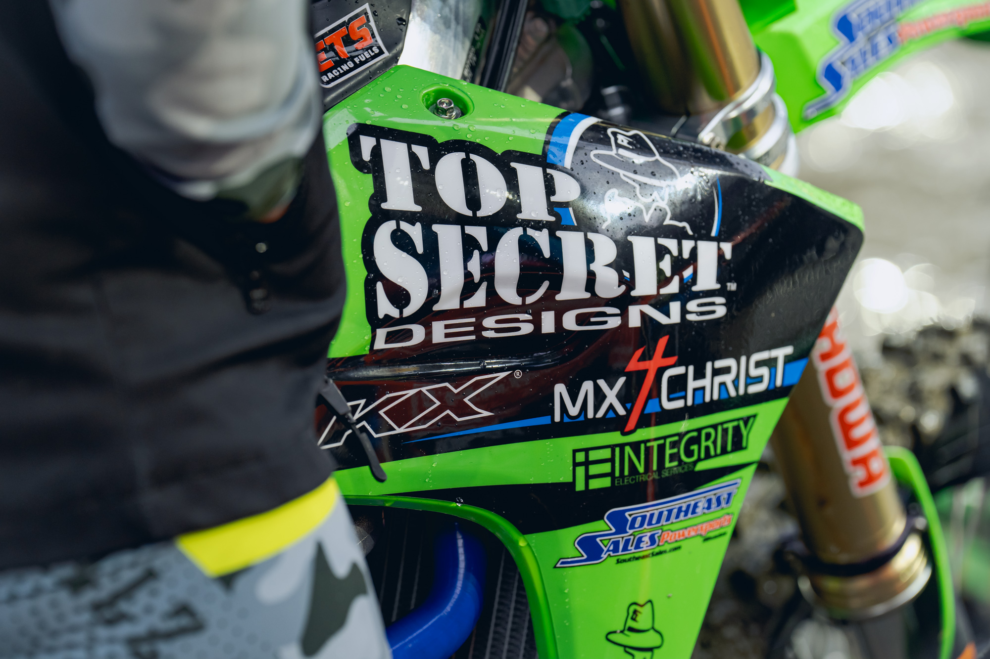 tight shot of the radiator shroud of the ISRT race bike. Team sponsor names, "Top Secret Designs", "MX 4 Christ", and more are ledgible on the shroud.