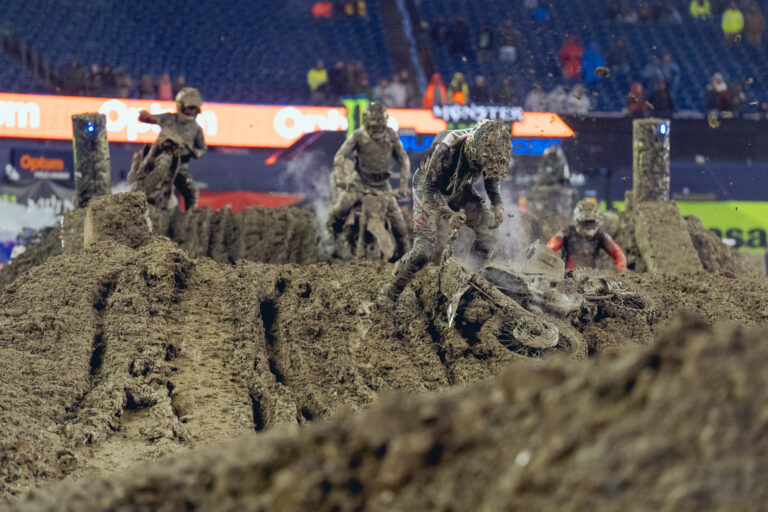 Image of muddy race track with dirt bike racers struggling to navigate the sticky dark brown gooey mess.