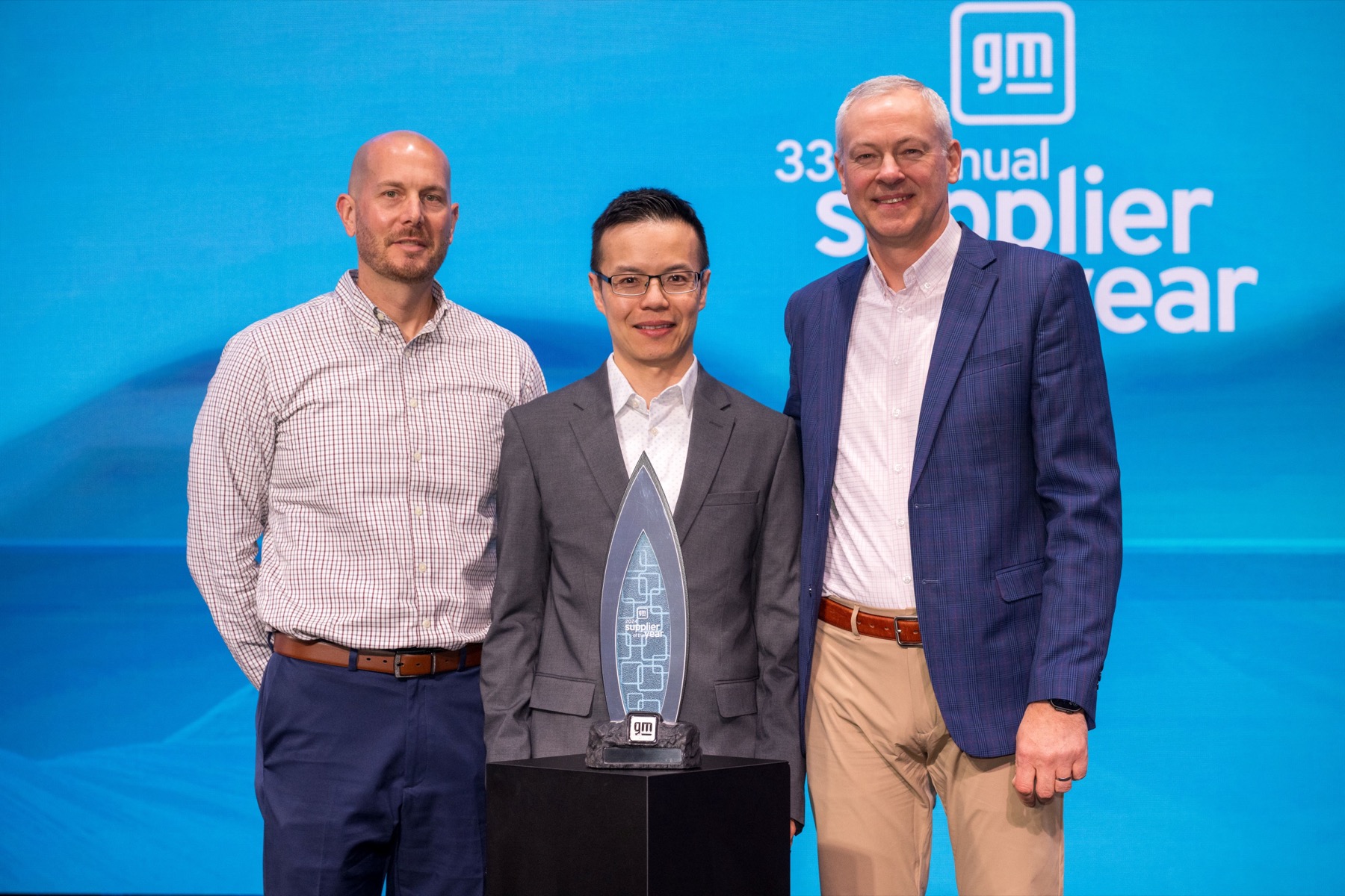 Three men standing behind a GM supplier of the year trophy.