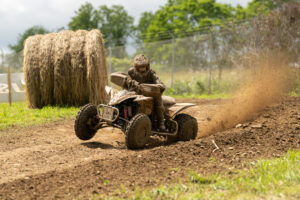 GNCC Maxxis athlete Hunter Hart once again staring down camera man Mack Faint while pinned exiting a flat corner. a tail of roost flying up in the background.