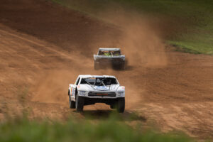 a white race truck blasting down a dirt hill with a competitor truck chasing in the distance.