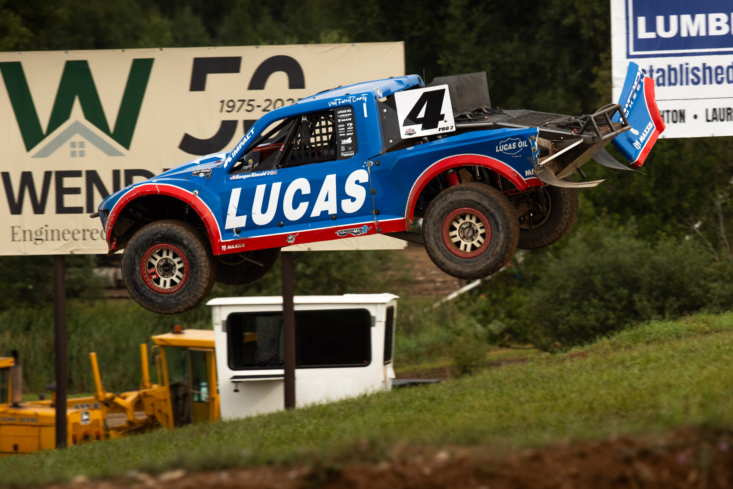 Keegan Kincaide in his blue and red Lucas oil truck flying down a hill over a large jump.