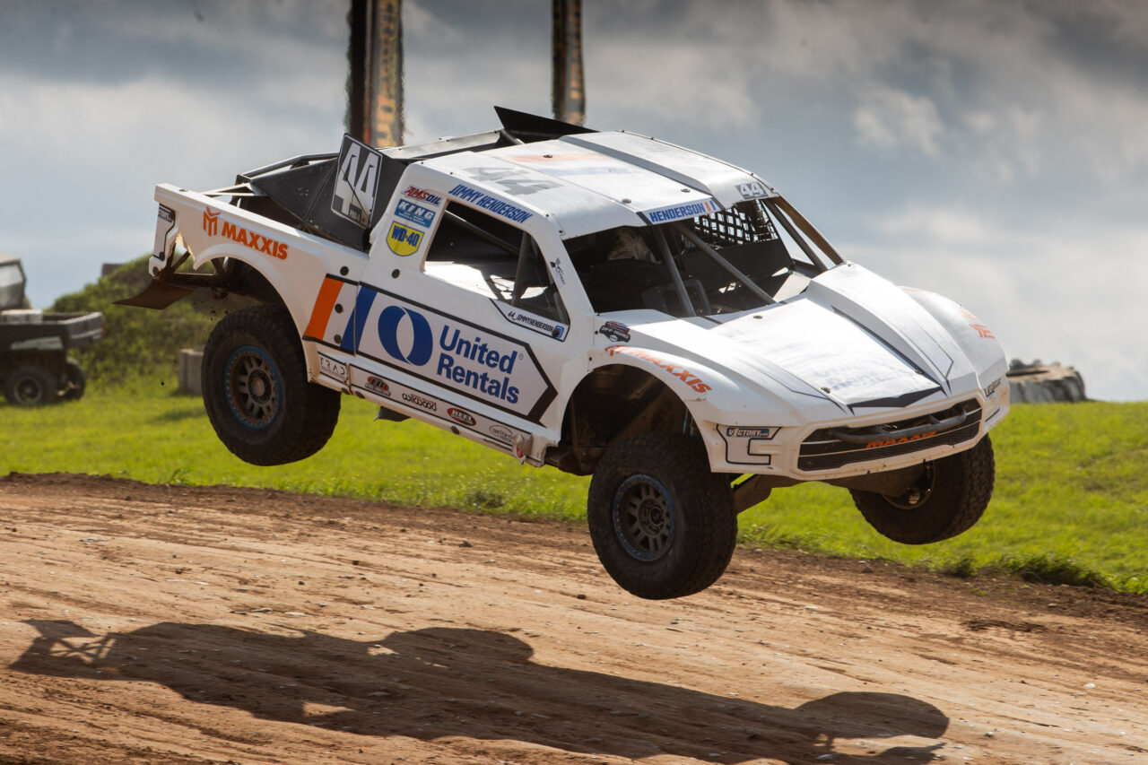 white truck about to land on the dirt of the race course.