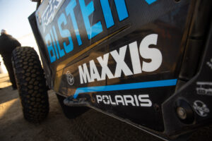 Close up of the driver side body panel of Doug Mittag's Polaris race car. the MAXXIS logo is displayed prominently in white.