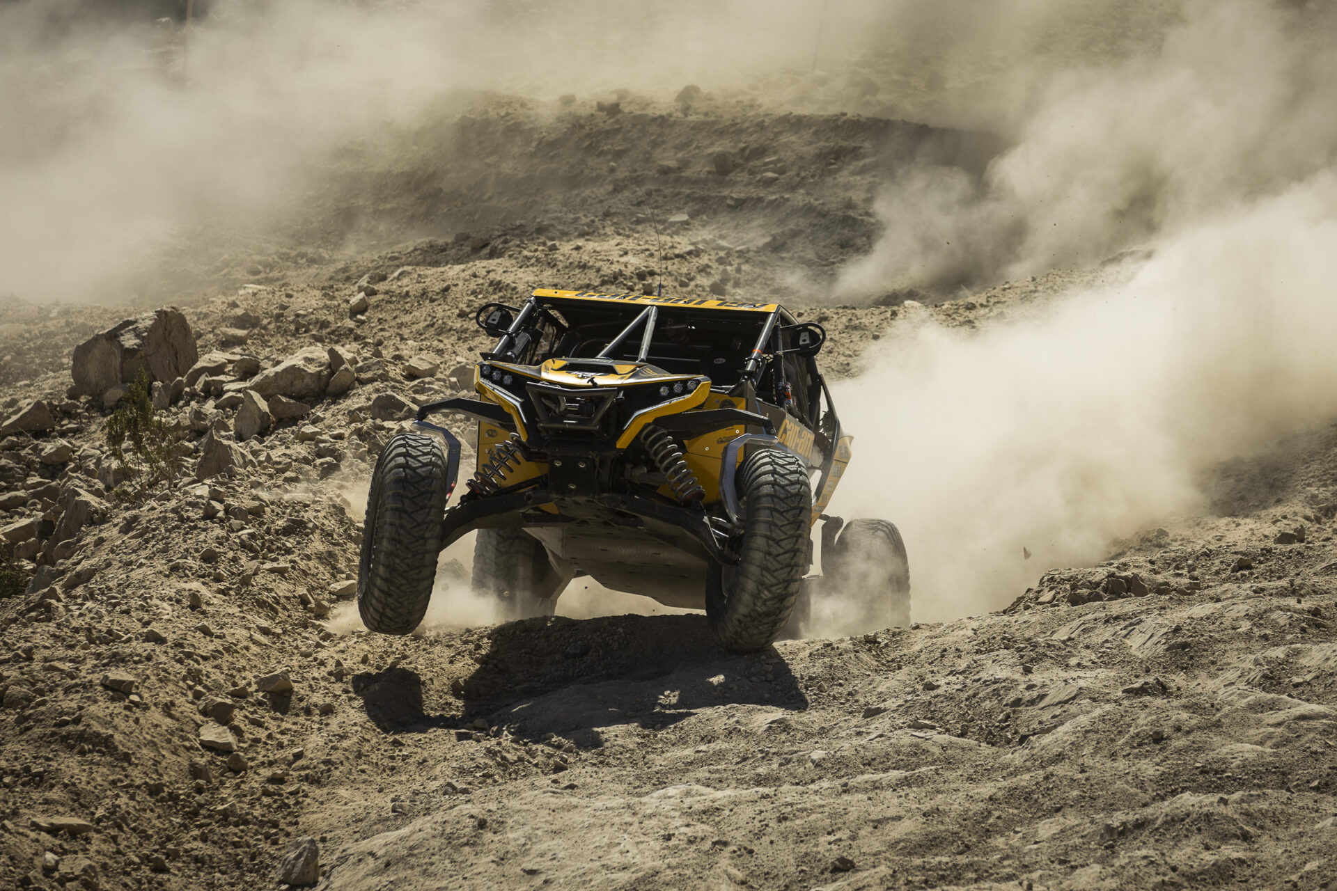 black and yellow Can Am SxS on it's back two wheels as it boosts over a rock lip.