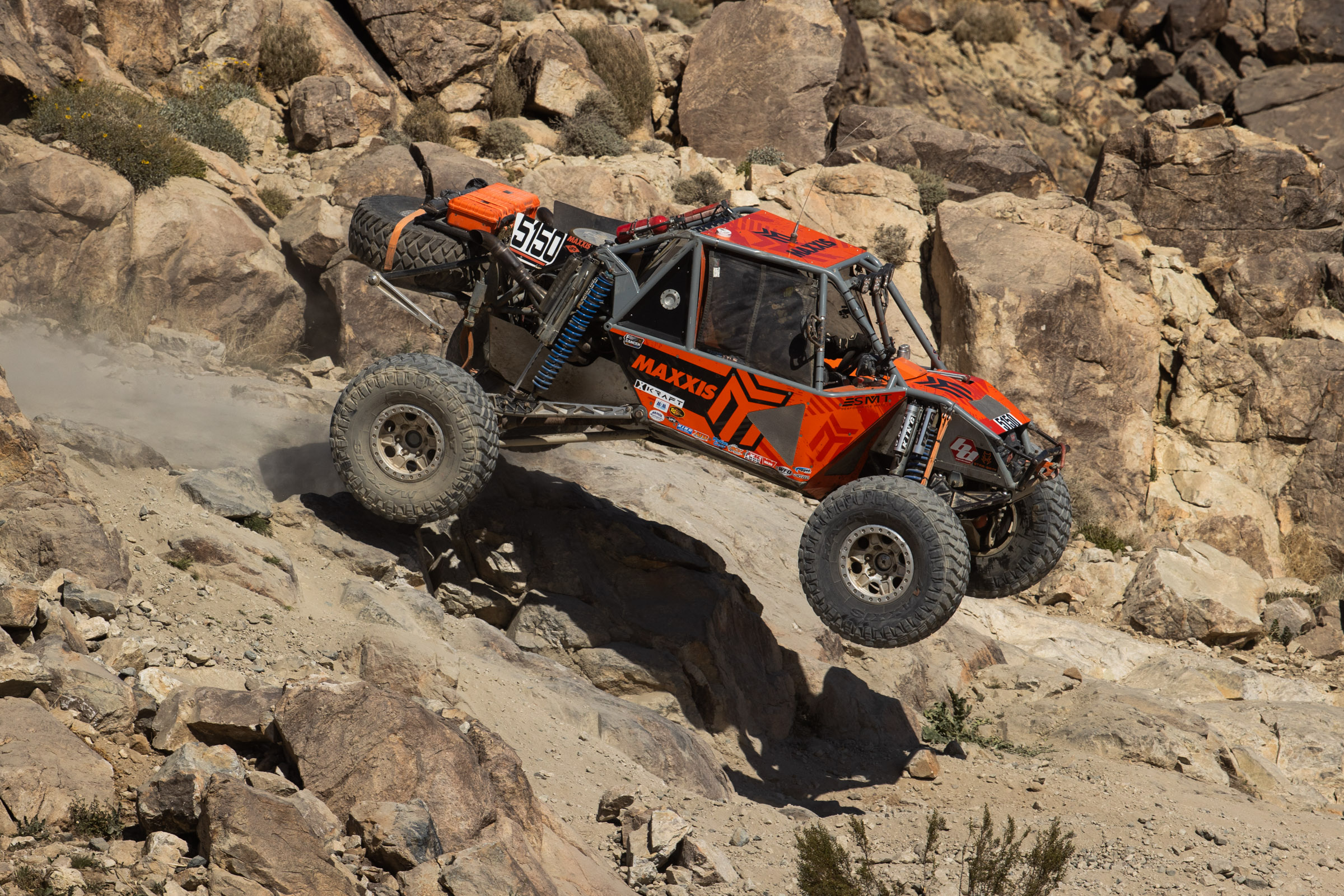 Brendon Thompson in his MAXXIS orange 4400 car blasting off of a popular rock feature called back door. 