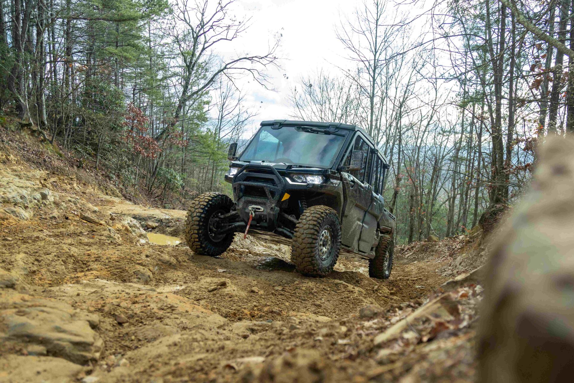 CanAm Defender going up a rocky Hill in the woods.