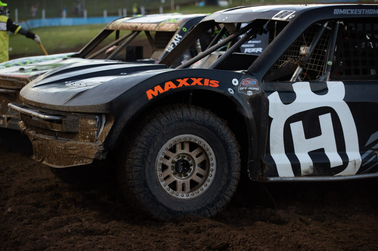 close up of the front half of a pro4 race truck. a bright orange MAXXIS logo is arched over the fender well.