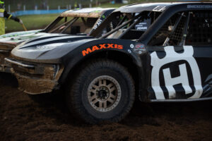 close up of the front half of a pro4 race truck. a bright orange MAXXIS logo is arched over the fender well.