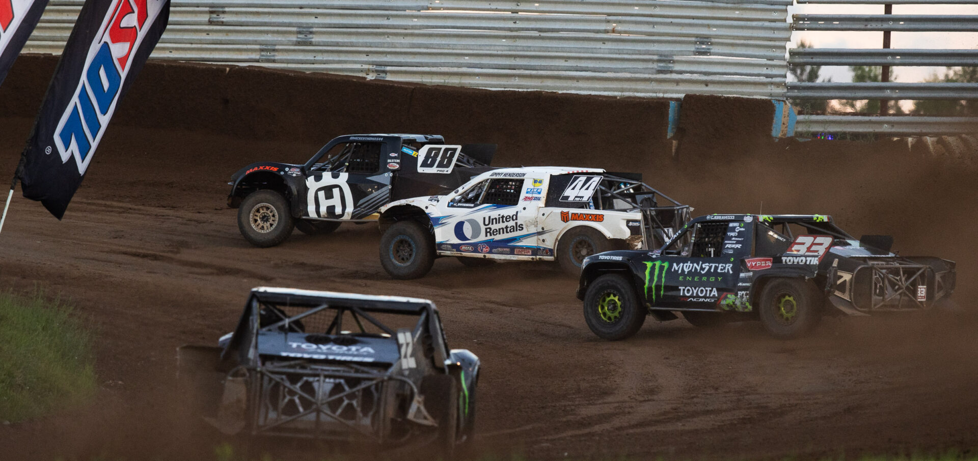4 short course race trucks in a left hand dirt turn.