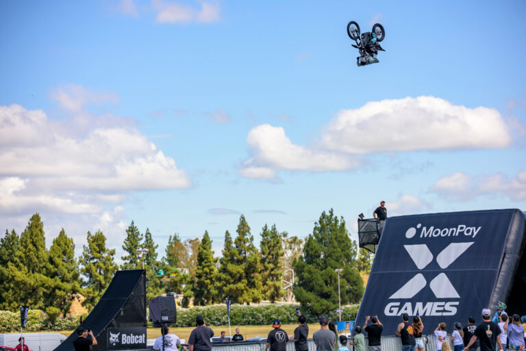 Dirt Bike Rider in mid-air flight. A black inflatable landing ramp is in view for the rider to land on.