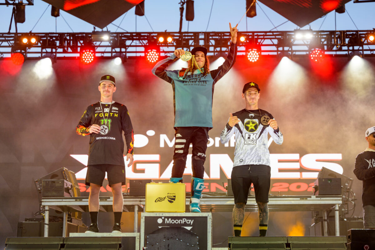 Pat Evans on the top step of the podium at X Games holding up a hand with his pointer and pinky finger extended in celebration.