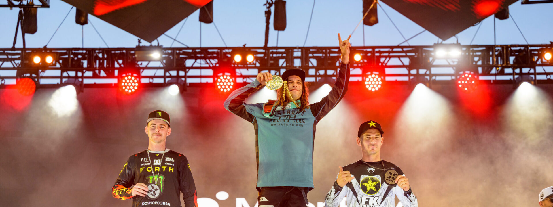 Pat Evans on the top step of the podium at X Games holding up a hand with his pointer and pinky finger extended in celebration.