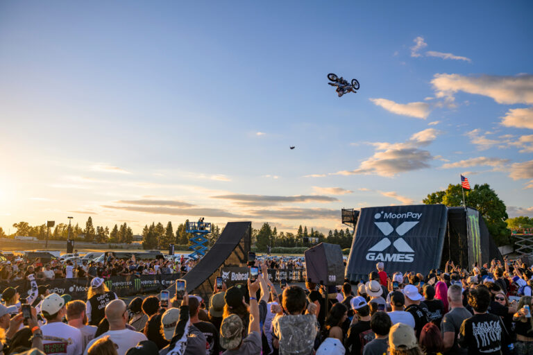 Dirt Bike Rider in mid-air flight. A black inflatable landing ramp is in view for the rider to land on.
