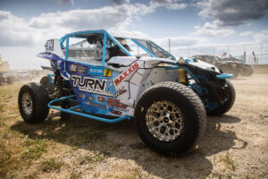 Blue and white off-road racing buggy parked on a dirt track under a cloudy sky.