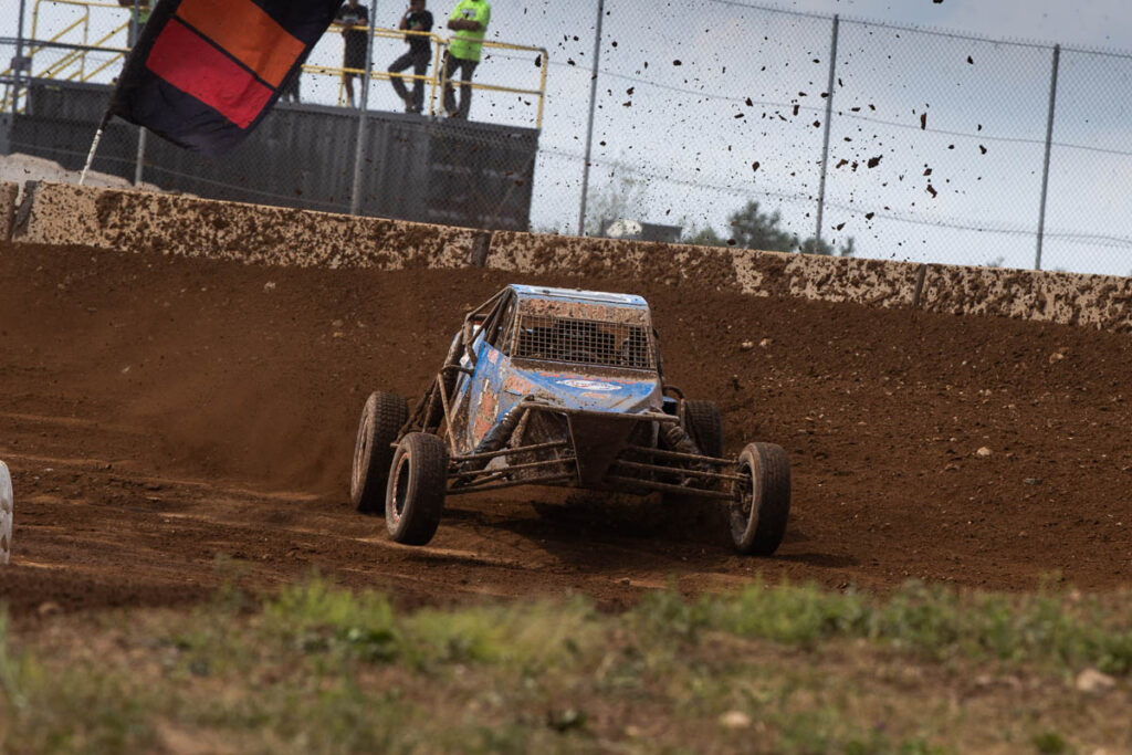 Blue off-road racing buggy aggressively navigating a dirt corner berm with loose soil flying.