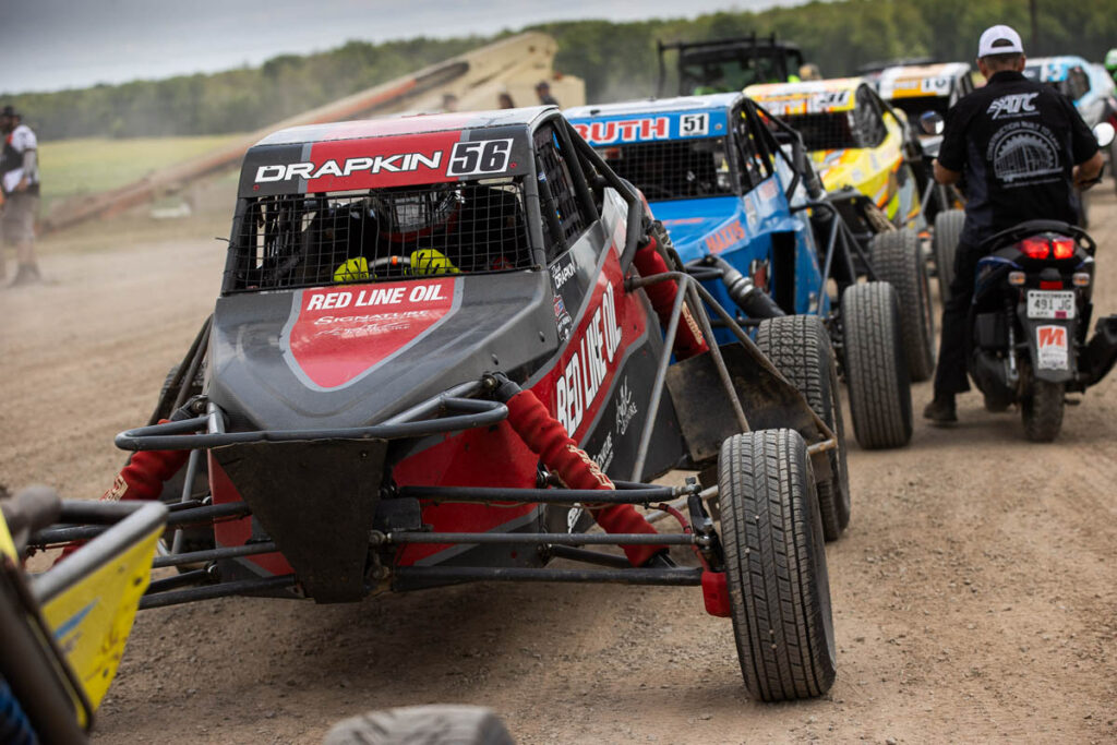 Line of off-road racing buggies queued up on a dirt track, featuring car number 56 in the foreground.