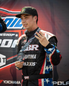 Connor Barry poses proudly with a 3rd-place medal and makes a three-finger gesture.