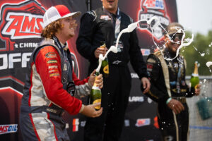 Zach Drapkin smiles on the podium while popping champagne with a 2nd-place medal.
